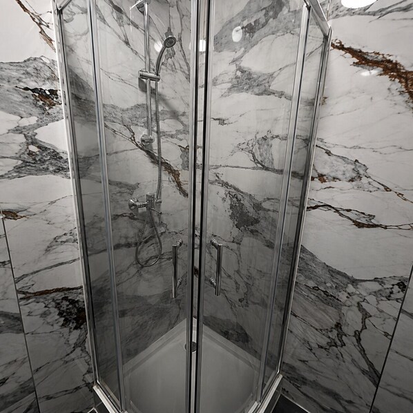 A glass-enclosed shower with a marble-tiled wall.