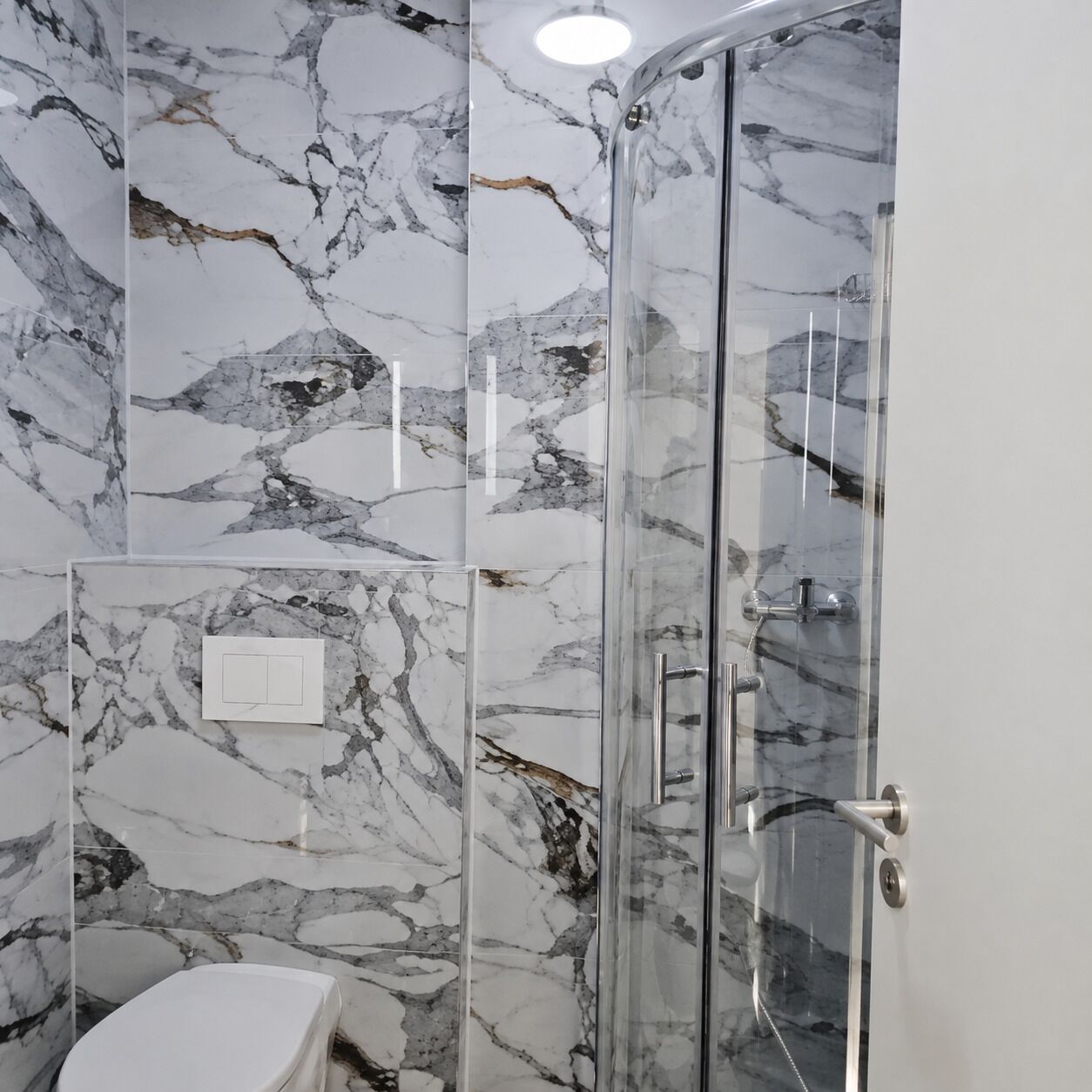 Ein Badezimmer mit einer gläsernen Duschkabine, Marmorwänden und einer weißen Toilette.