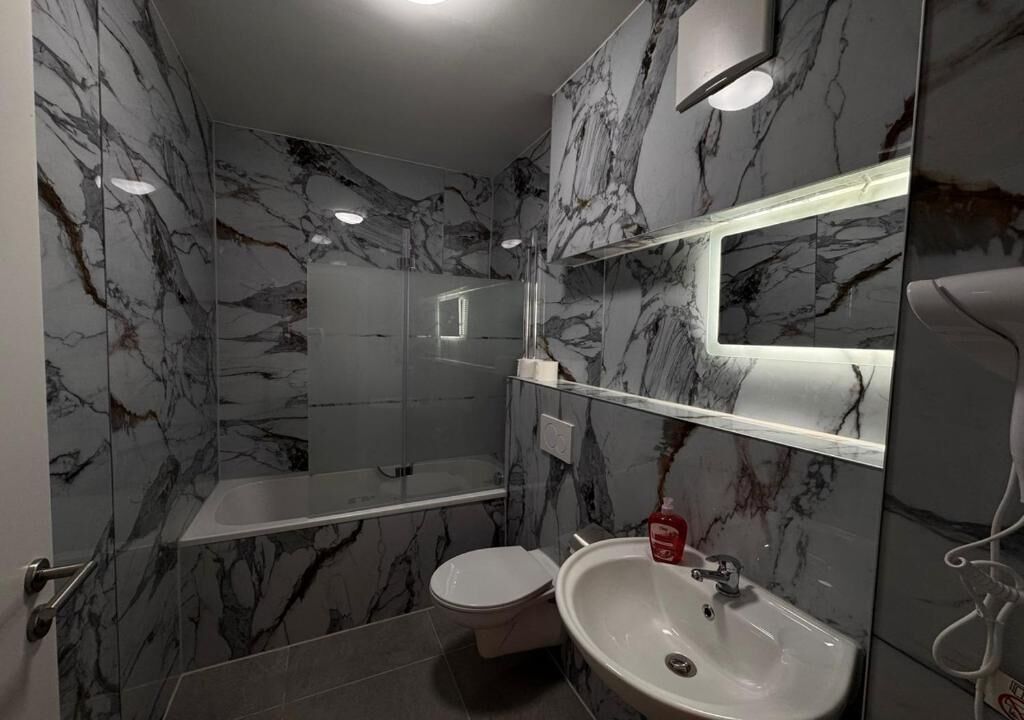 A bathroom with a marble wall, a toilet, a sink, and a shower area.