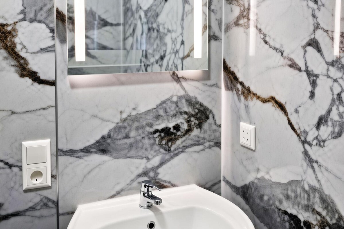 Un baño con lavamanos de mármol y un espejo con una tira de luz vertical.