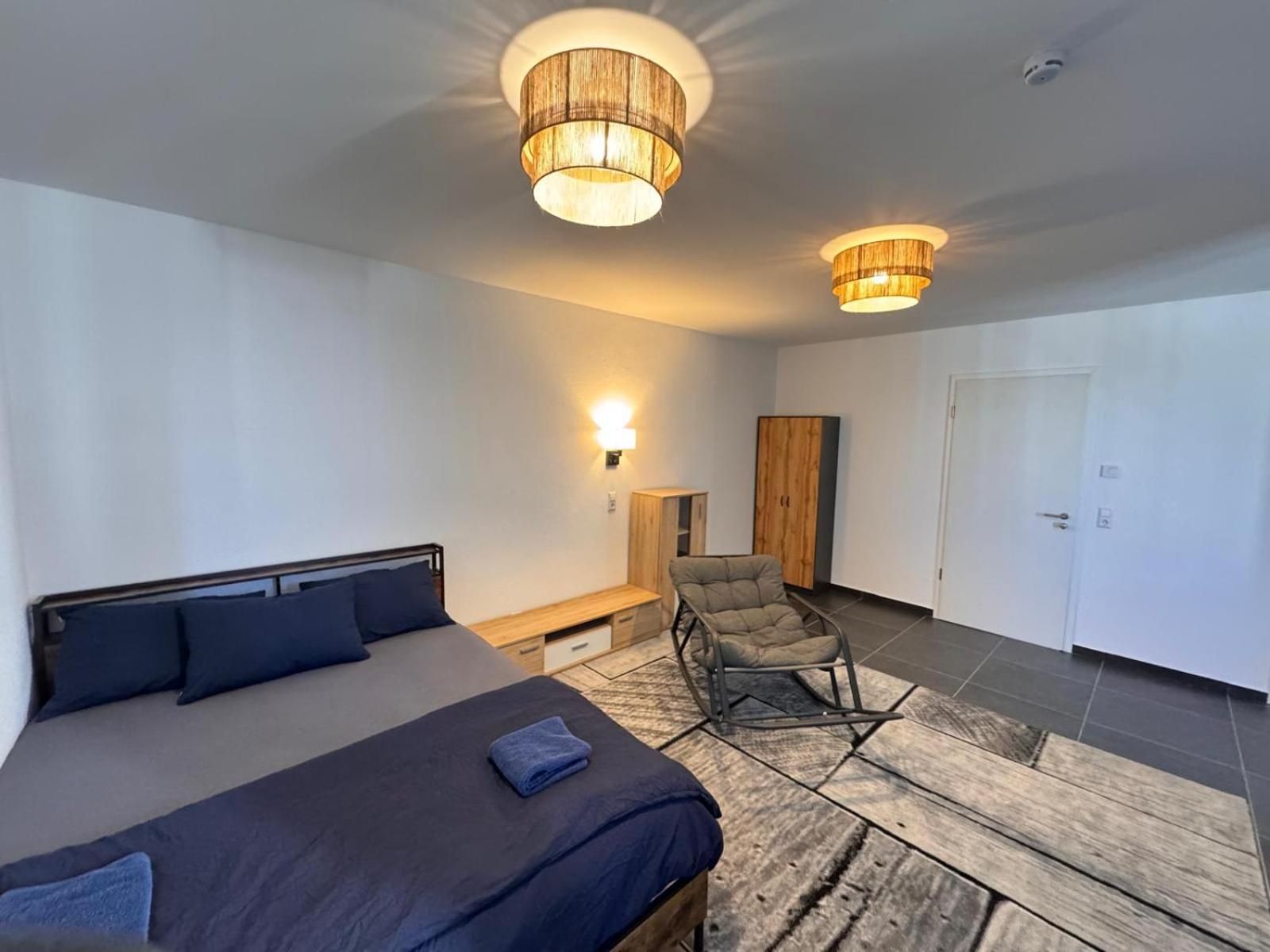 Un dormitorio moderno con una cama grande, una silla, un armario y dos lámparas colgantes.