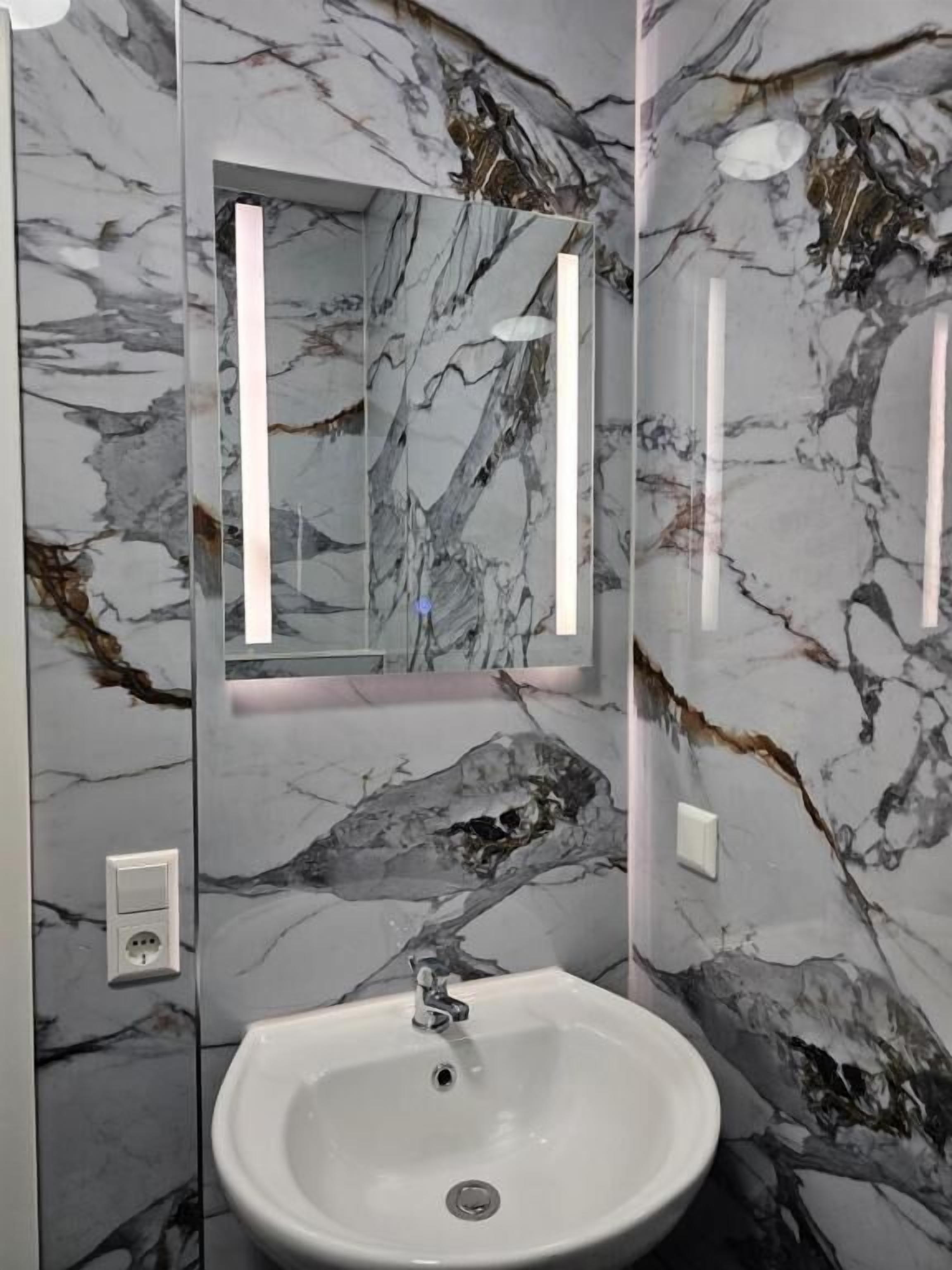 Ein Badezimmer mit Marmorwand, einem weißen Waschbecken und einem Spiegel.