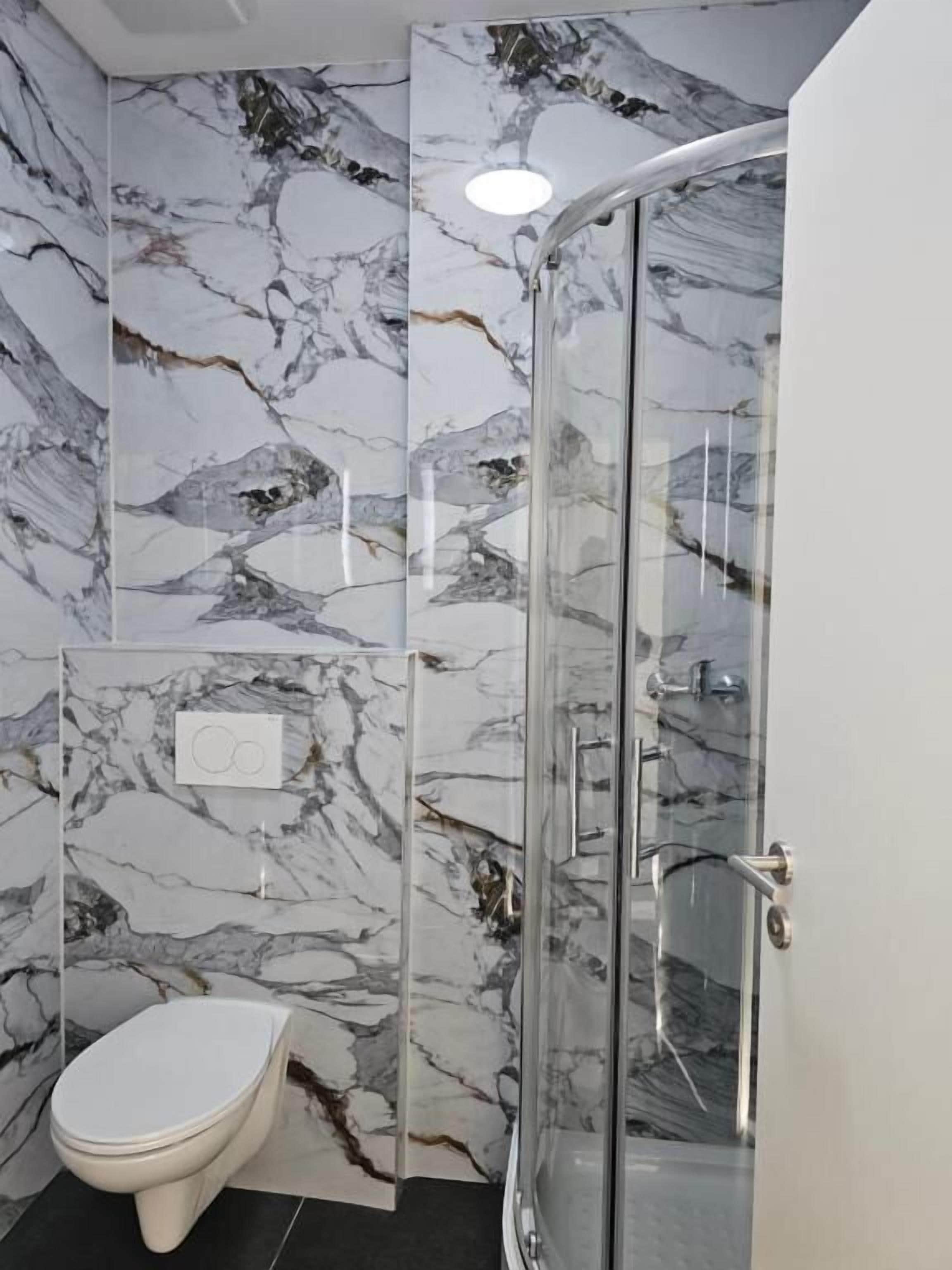 A bathroom with a toilet, a glass shower enclosure, and marble walls.