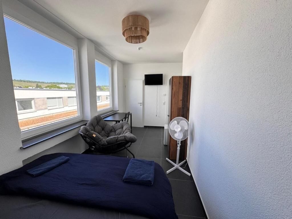 Una habitación con cama, una silla, un televisor y un ventilador.