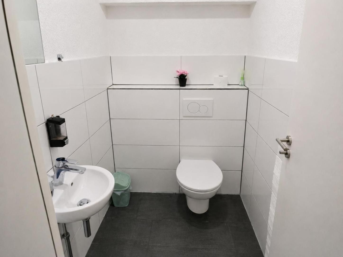 A small, compact bathroom with a white sink, toilet, and a small trash bin.