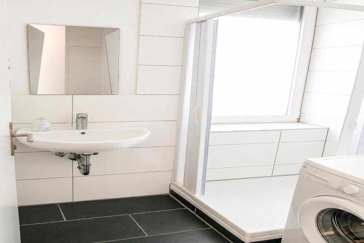 Un baño con lavabo, espejo, ducha y lavadora.