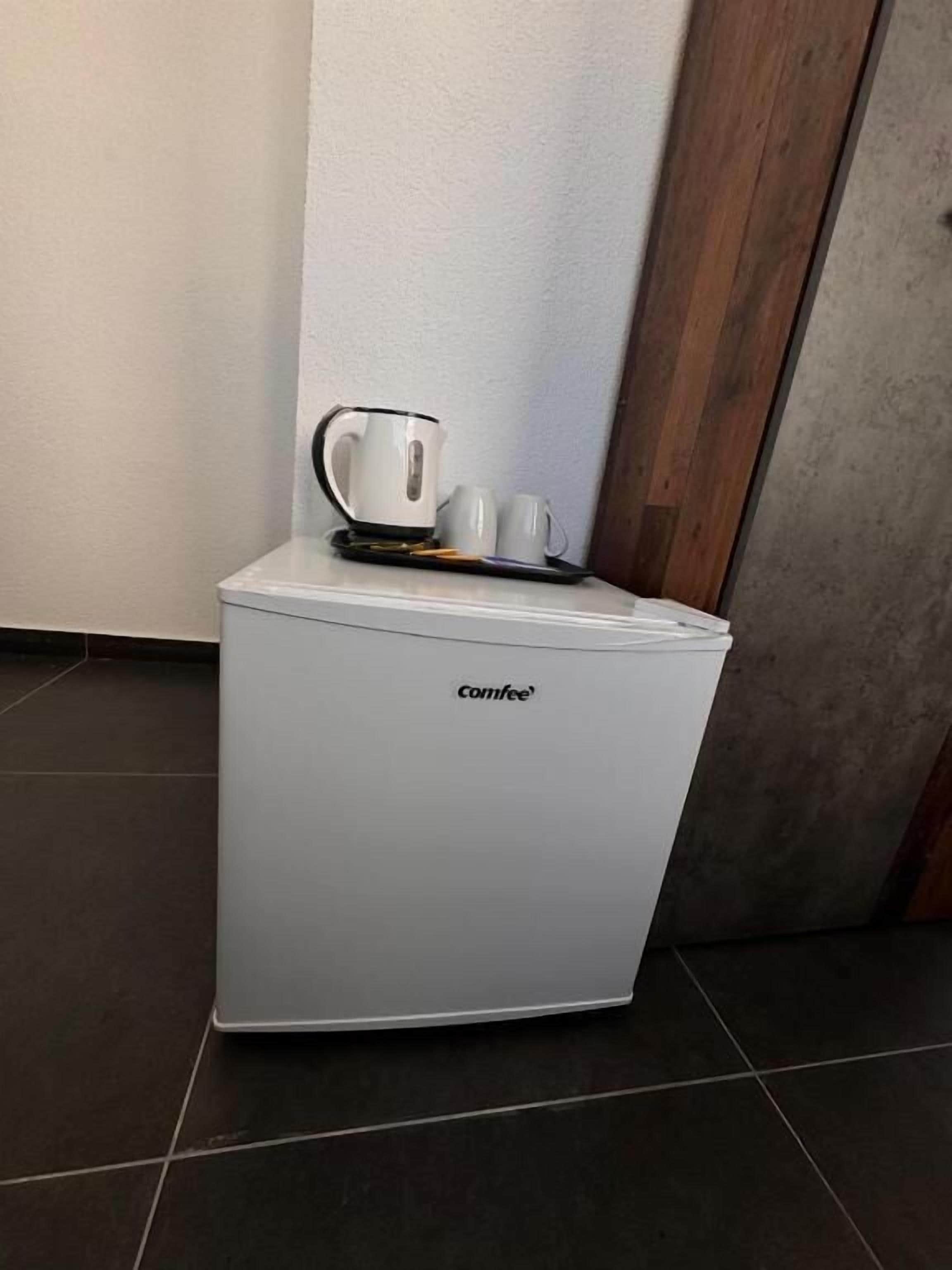 A compact coffee machine with a white exterior, placed on a tiled floor against a wall with a wooden panel.