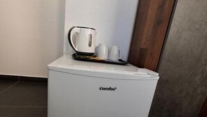 Una cafetera compacta de color blanco, sobre un suelo de baldosas frente a una pared con paneles de madera.