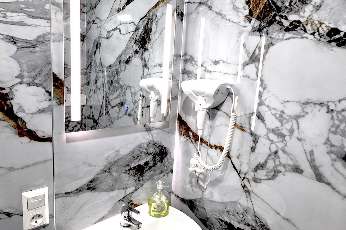 Un baño con pared de mármol, lavamanos, espejo y secador de pelo.