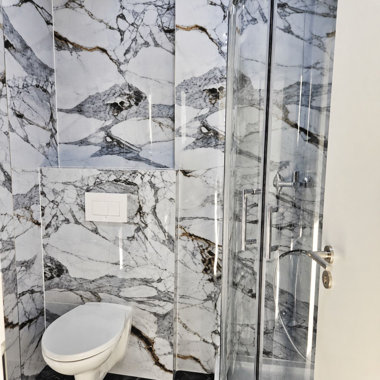 A bathroom with a marble wall, a toilet, and a glass-enclosed shower area.