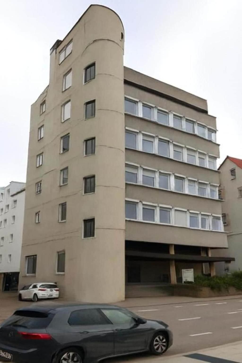 Ein mehrstöckiges Gebäude mit einer gebogenen Ecke, einer schlichten Fassade und einer Reihe von Fenstern.