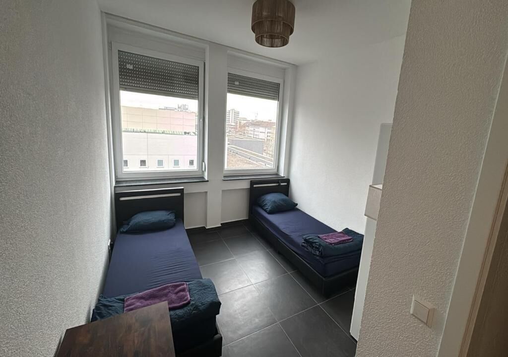 Una habitación pequeña con dos camas, una ventana y una puerta.