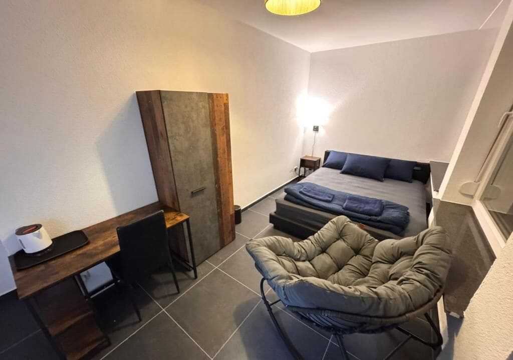 Una habitación de hotel pequeña con una cama, una silla, un escritorio y un armario.