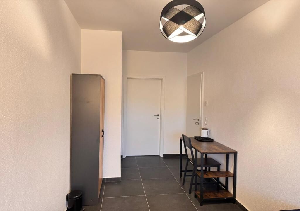 Ein Flur mit einer Tür, einem Mülleimer, einem Tisch mit Stühlen und einer Pendelleuchte.