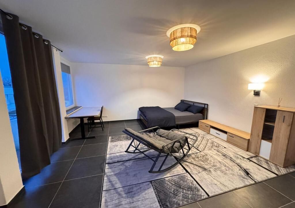 A modern bedroom with a bed, a rocking chair, a desk, and a lamp.