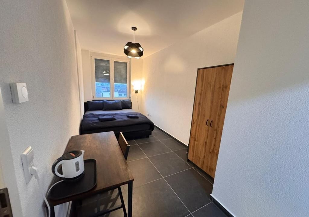 Ein kleines Zimmer mit einem Bett, einem Tisch mit Wasserkocher, einem Kleiderschrank und einem Fenster mit Blick.