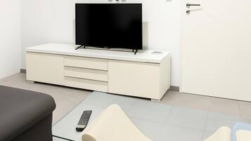 A modern room with a flat-screen TV on a white cabinet, a glass coffee table with a remote, and a door with a handle.