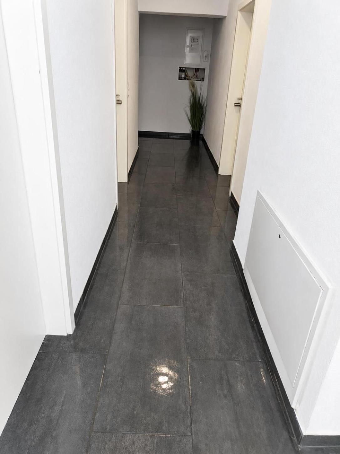 A corridor with dark tiled flooring, white walls, and a door on the left.