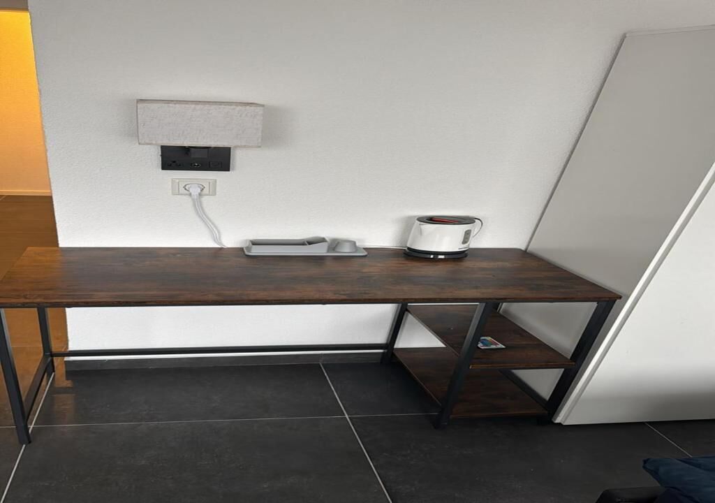 A corner desk with a coffee maker, a power outlet, and a shelf.
