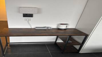 A corner desk with a coffee maker, a power outlet, and a shelf.