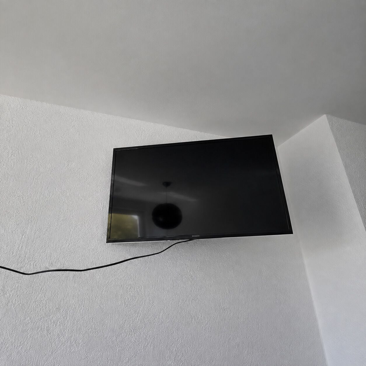 A flat-screen TV mounted on a white wall with a visible cable.