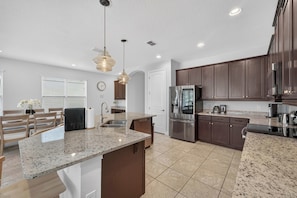 A modern kitchen with granite countertops, stainless steel appliances, and dark wooden cabinets. - 5BR Encore Sleeps 12 w/ Pool, Spa & Game Tables (Kissimmee)