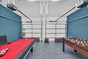 A pool table with a red felt surface, a foosball table, and a billiards cue rack. - 5BR Encore Sleeps 12 w/ Pool, Spa & Game Tables (Kissimmee)
