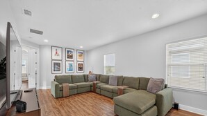 Ein modernes Wohnzimmer mit einem Ecksofa, Holzboden und gerahmten Kunstwerken an der Wand.