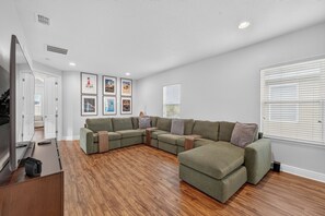 Ein modernes Wohnzimmer mit einem Ecksofa, Holzboden und gerahmten Kunstwerken an der Wand.