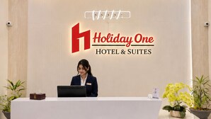 A hotel reception desk with a sign reading 'Holiday One Hotel & Suites.'