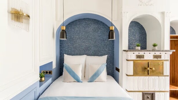 A bedroom with a bed, a blue textured wall, two black pendant lights, a white fireplace with gold trim, and a small plant on the mantel. - Spectacular 6 bedroom in the Heart of the Opéra District (Paris)