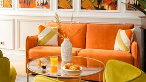 A room with an orange sofa, a glass coffee table, and a vase with dried plants. - Spectacular 6 bedroom in the Heart of the Opéra District (Paris)