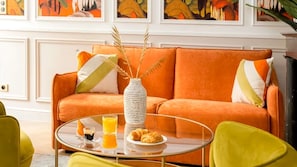 A room with an orange sofa, a glass coffee table, and a vase with dried plants. - Spectacular 6 bedroom in the Heart of the Opéra District (Paris)
