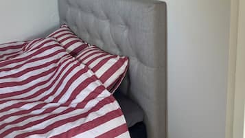 A bedroom with a bed, a headboard, a wall-mounted lamp, and a power outlet.