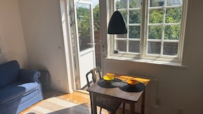 A room with a blue sofa, a wooden table with two bowls, a hanging lamp, and a window with a view of greenery.