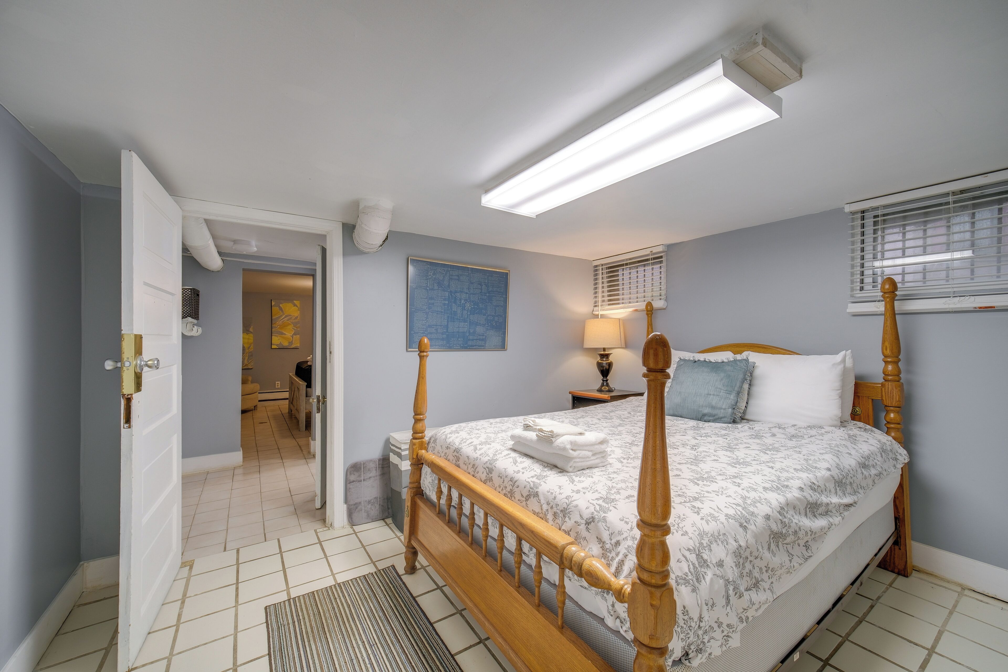 A bedroom with a four-poster bed, a nightstand with a lamp, and a window with blinds.