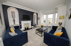 Ein Wohnzimmer mit zwei blauen Sofas, einem Kamin, einem Fernseher und einem großen Fenster.