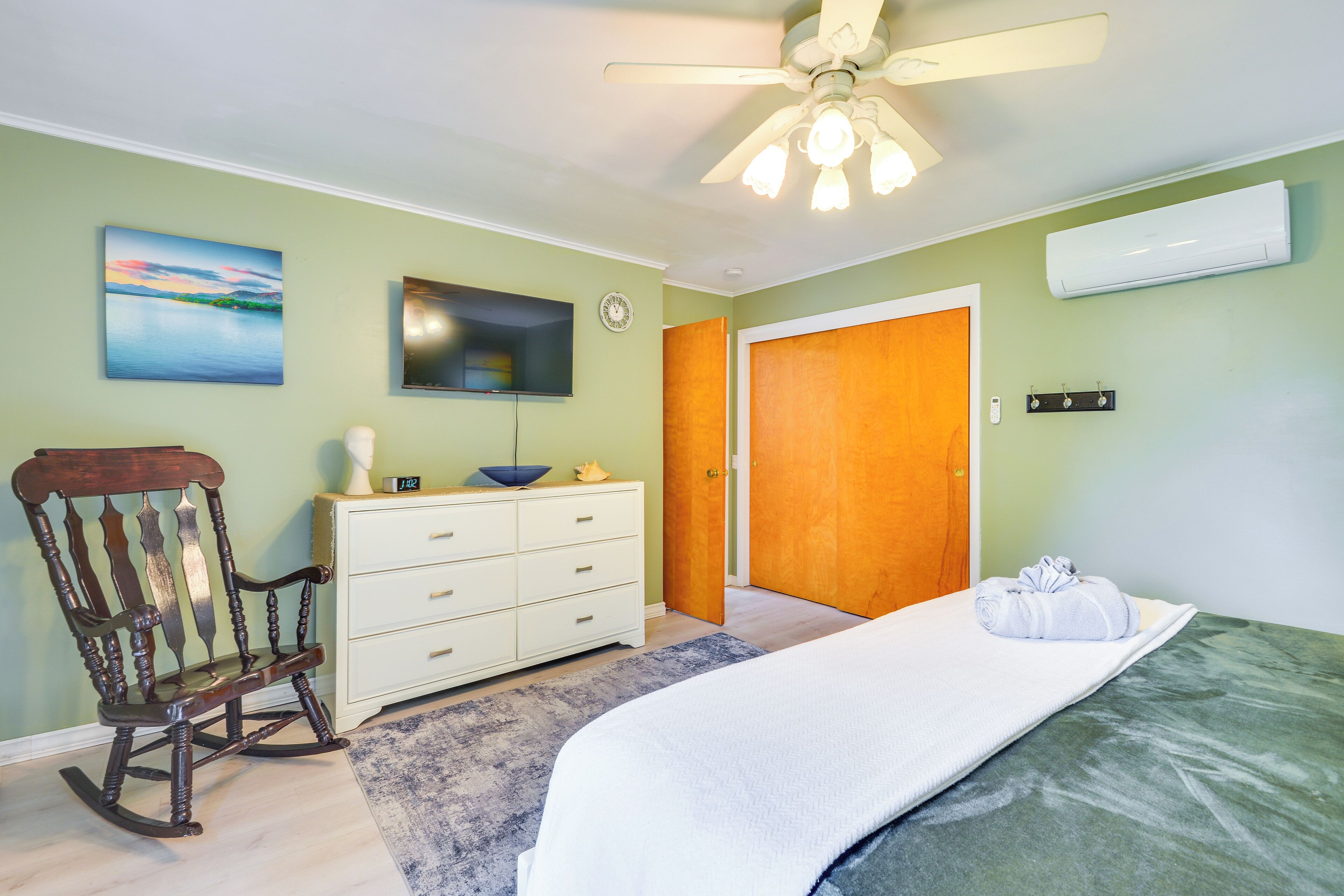 A bedroom with a bed, a rocking chair, a dresser, a television, and a ceiling fan.
