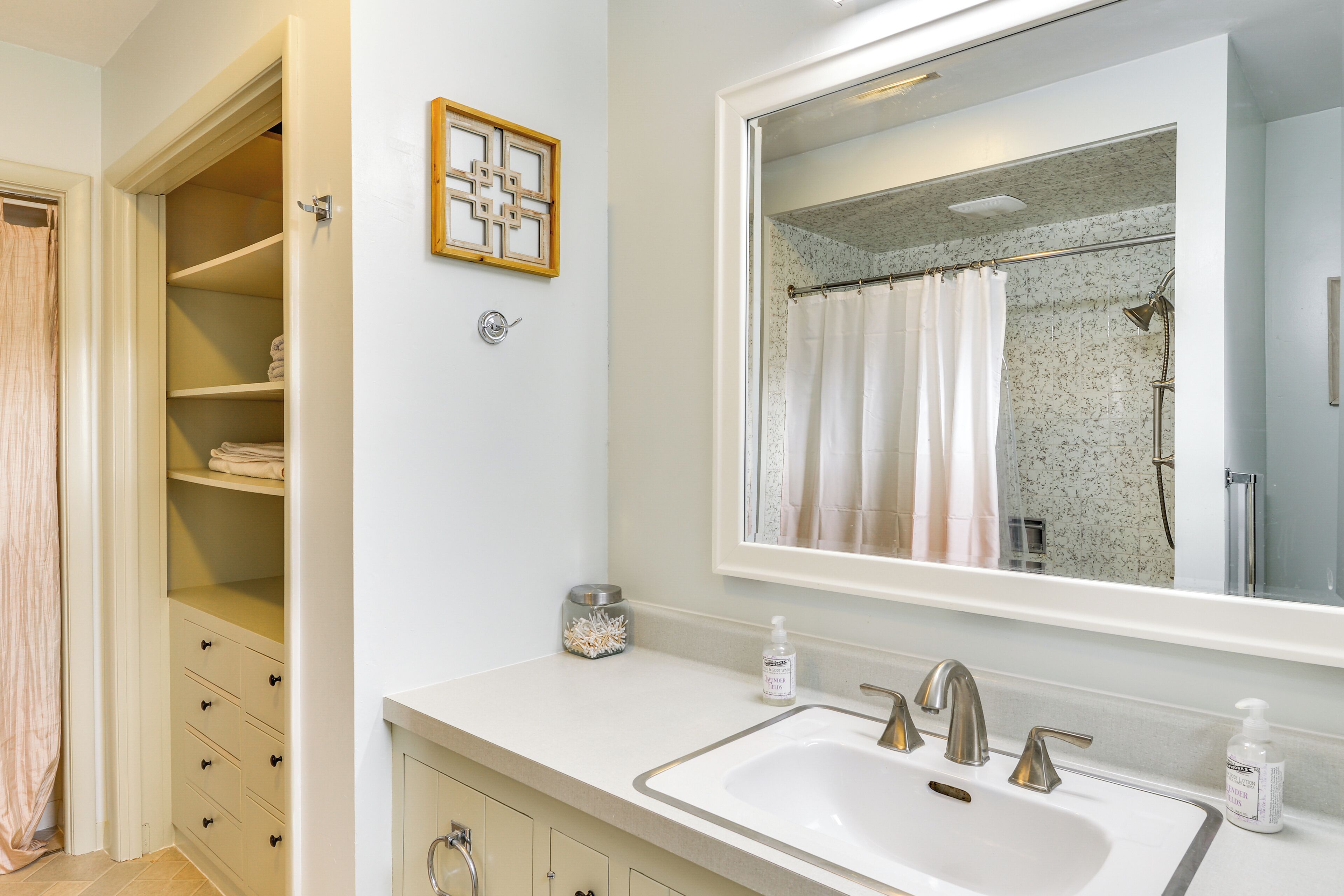 A bathroom with a white sink, two faucets, a large mirror, and a shower curtain.