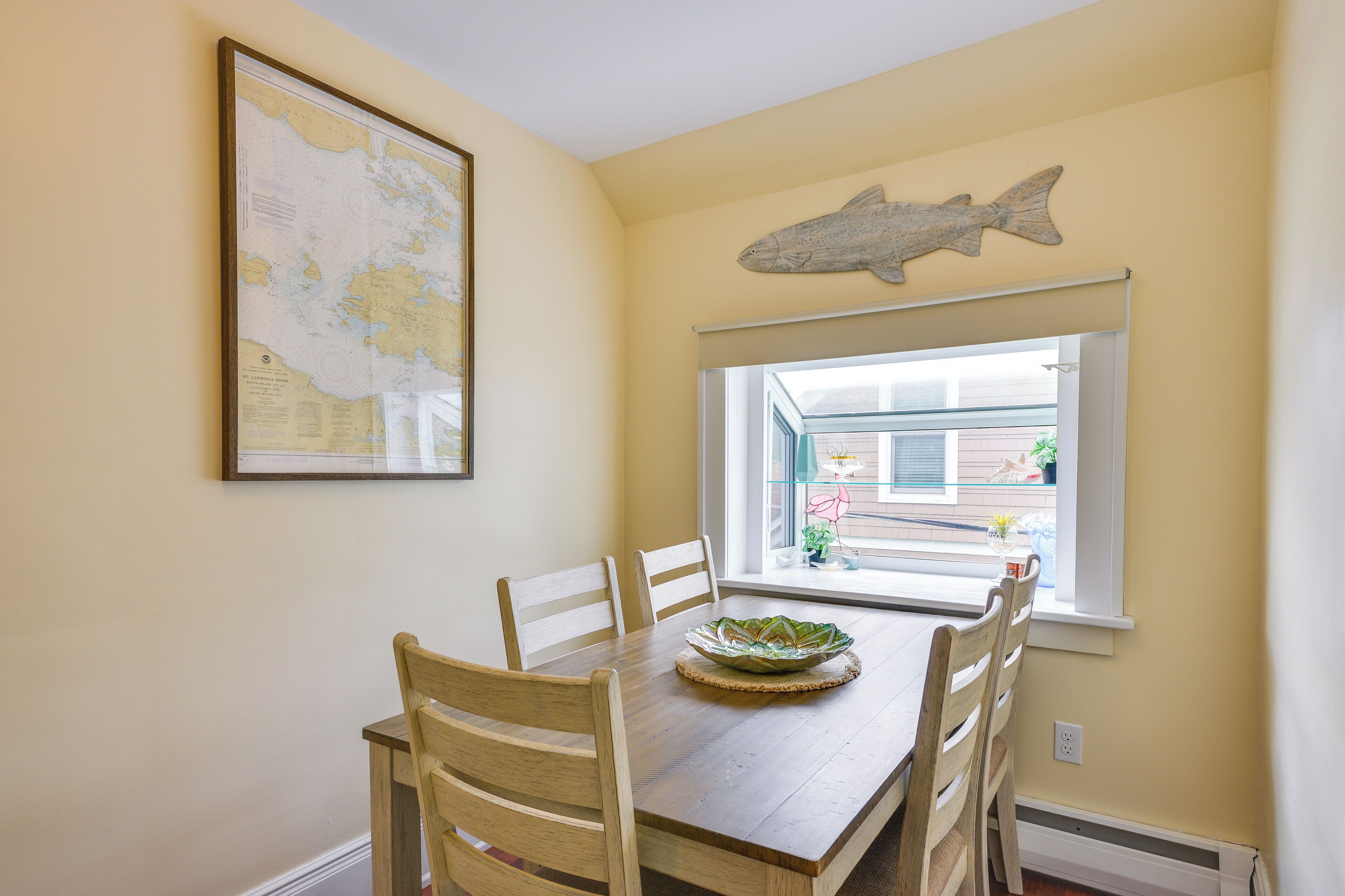 Un comedor con una mesa de madera, seis sillas, un pez decorativo en la pared y un mapa en la pared.