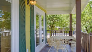 A covered porch with a table and chairs, a door with a window, and a railing.