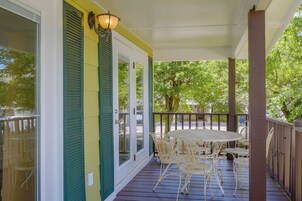 A covered porch with a table and chairs, a door with a window, and a railing.