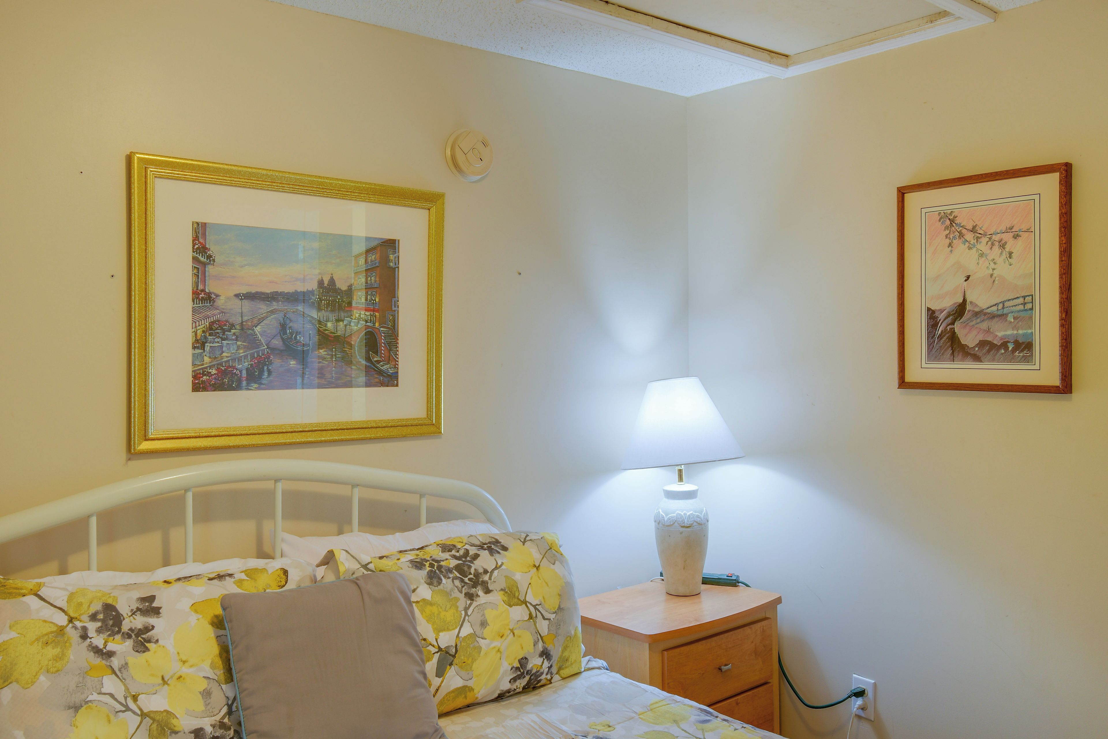 A bedroom with a bed, a nightstand with a lamp, and two framed pictures on the wall.
