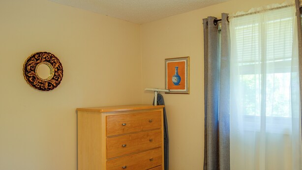 A bedroom with a wooden dresser, a framed picture on the wall, and a window with curtains. - Walk to Beach! Water-view Fairhope Retreat (Fairhope)