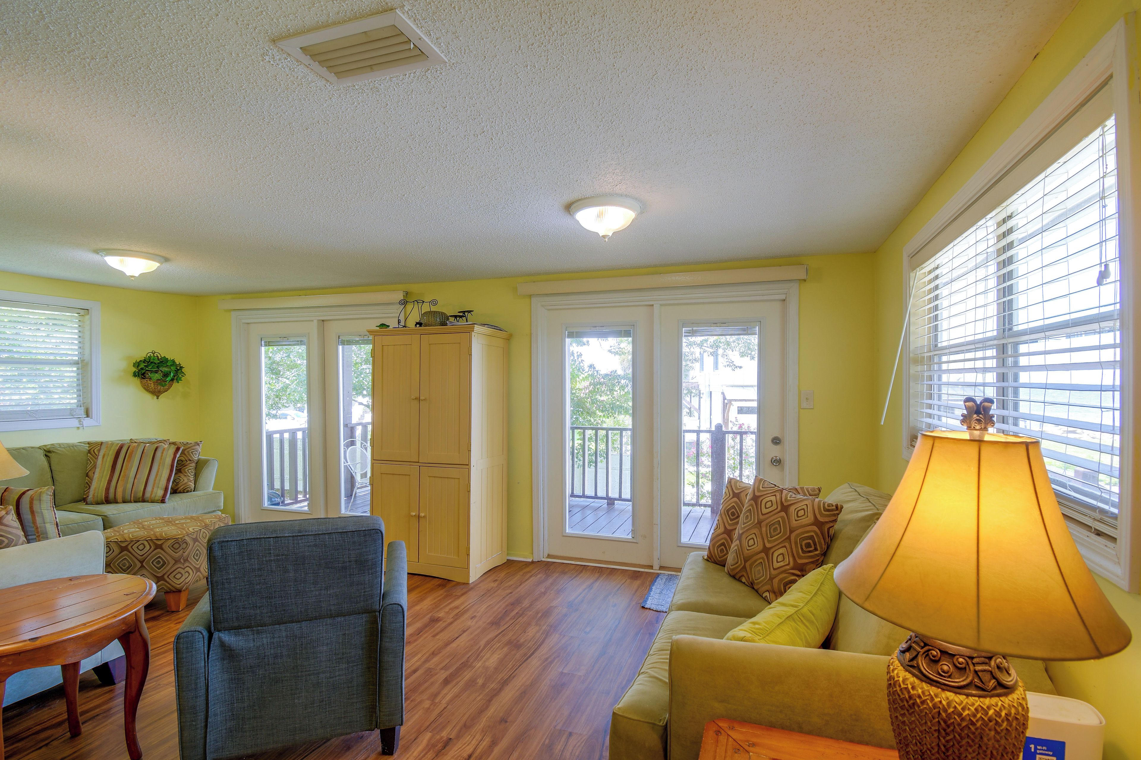A living room with a sofa, armchair, and a lamp. There are two doors leading to a balcony.
