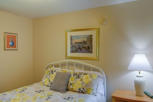 Un dormitorio con una cama, una mesita de noche con lámpara y dos cuadros en la pared.