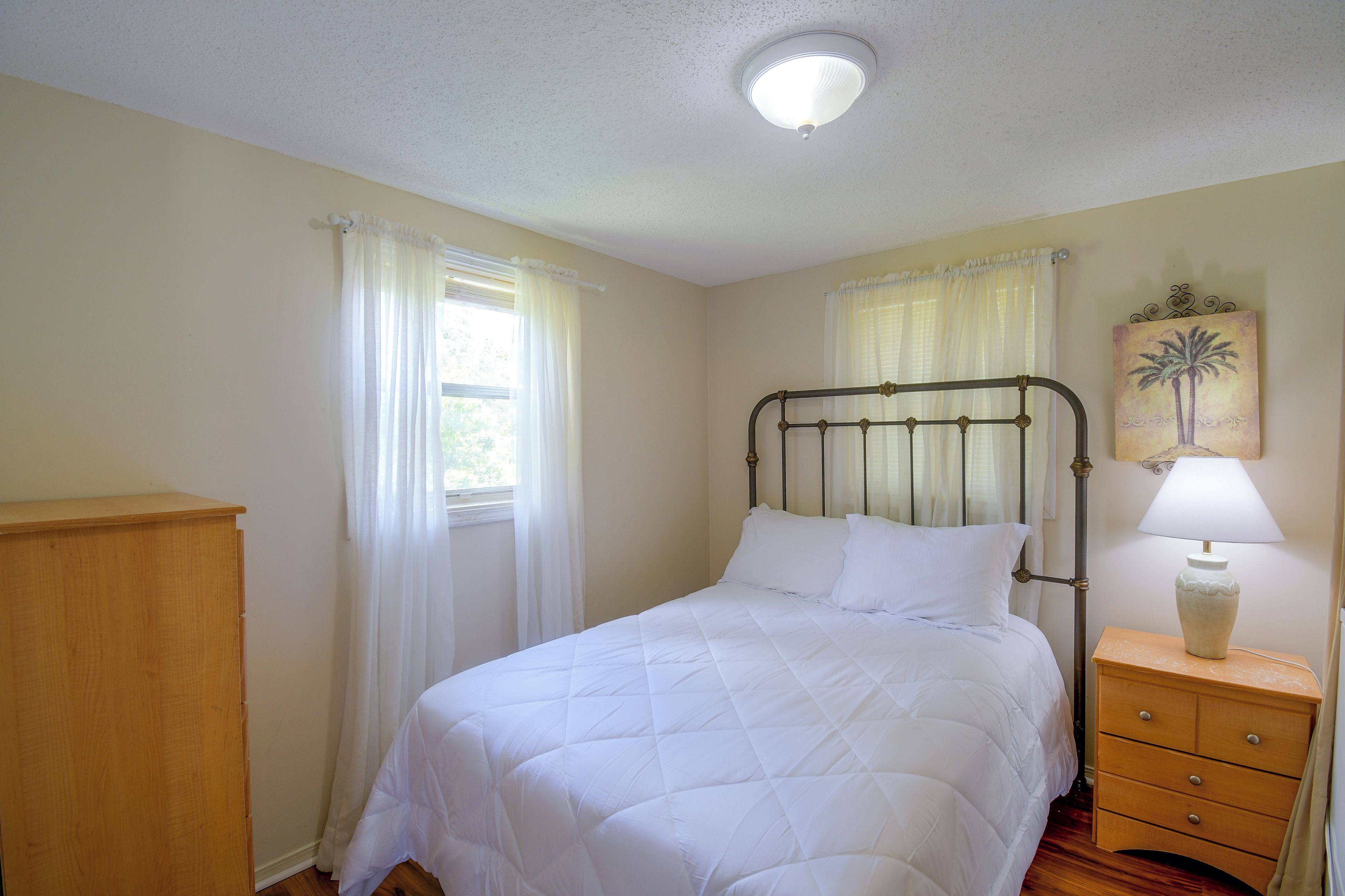 A bedroom with a bed, a nightstand, a lamp, a wooden dresser, and a ceiling light fixture.