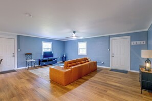 Ein geräumiges Wohnzimmer mit Holzdielenboden, einem großen orangefarbenen Sofa, einem Flachbildfernseher und einem Deckenventilator.