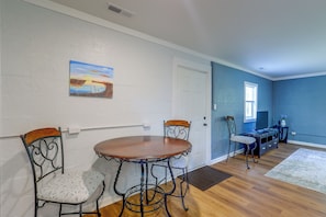 A dining area with a round table and four chairs, a painting on the wall, and a blue accent wall.