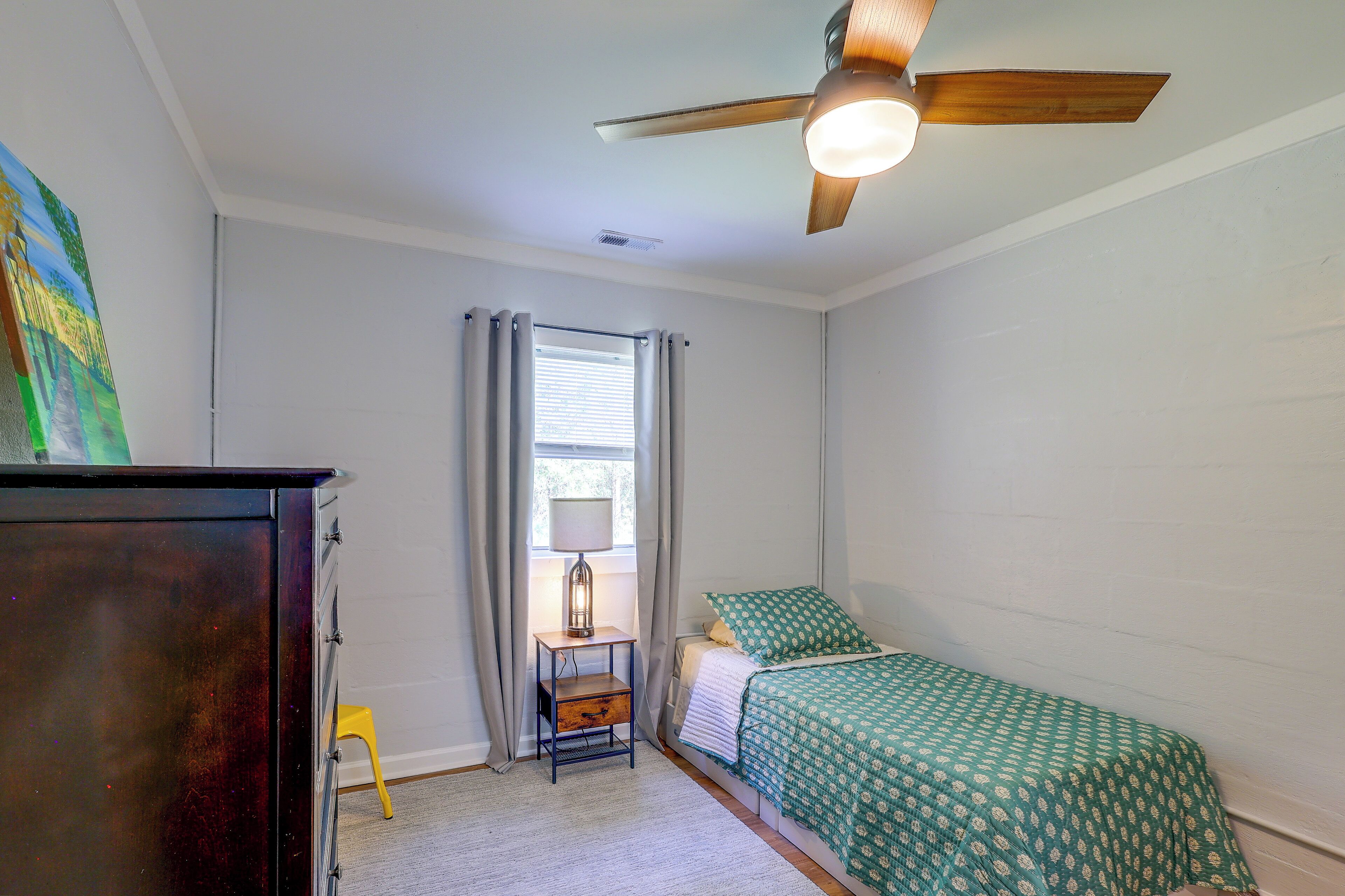 A bedroom with a bed, a nightstand, a ceiling fan, and a window with curtains.